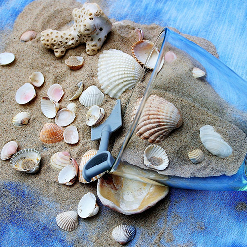 Glass of sand and sea shells on blue table